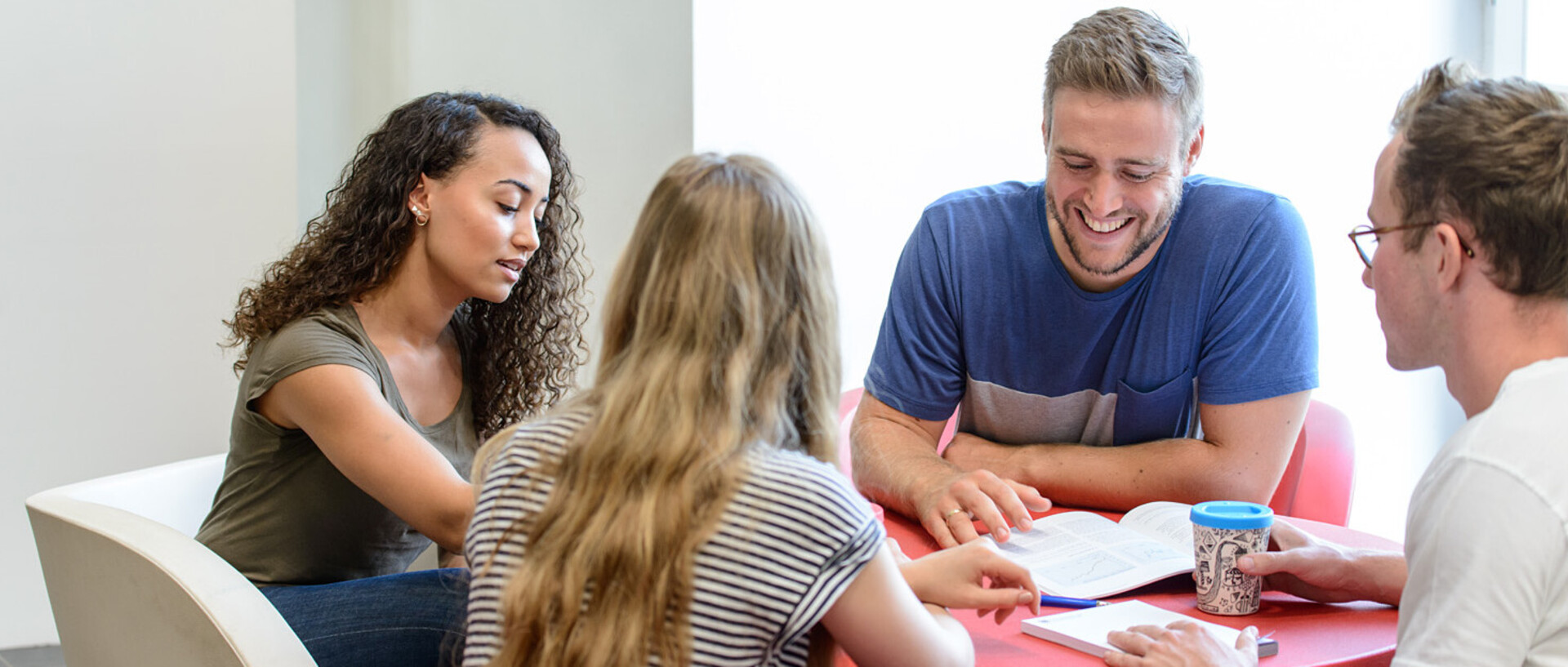 Vier Studierende sitzen an einem roten, runden Tisch und lernen gemeinsam.